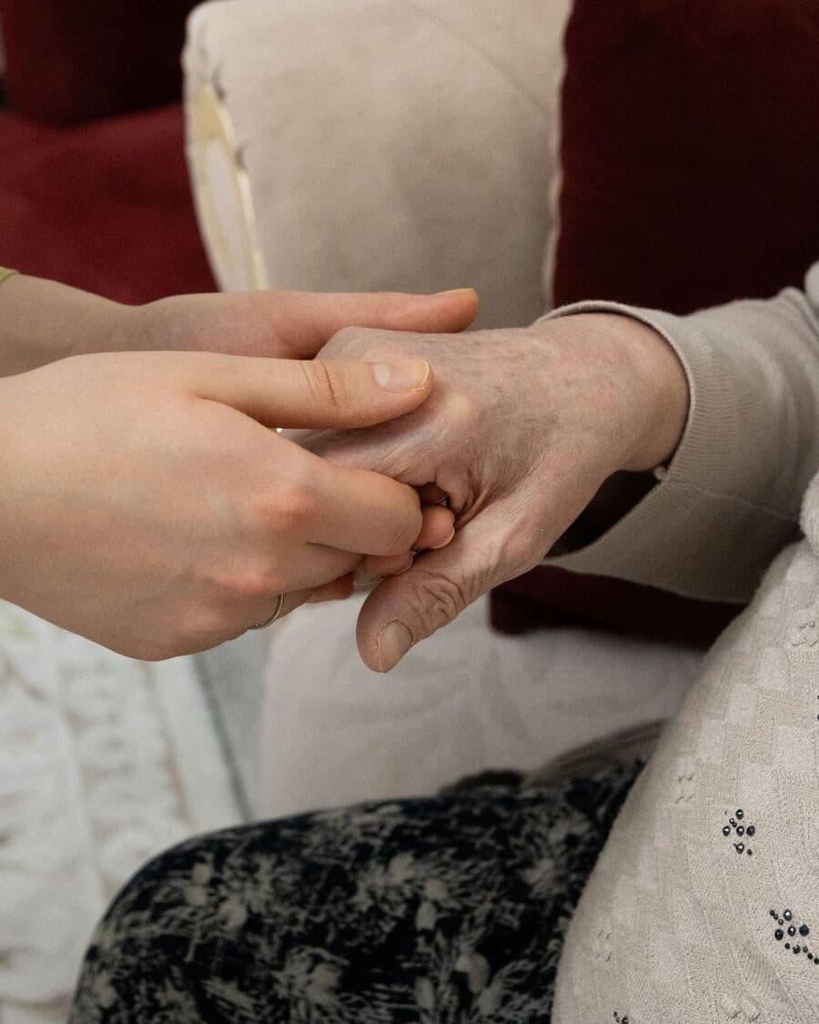 A younger person's hands gently holding an older person's hand