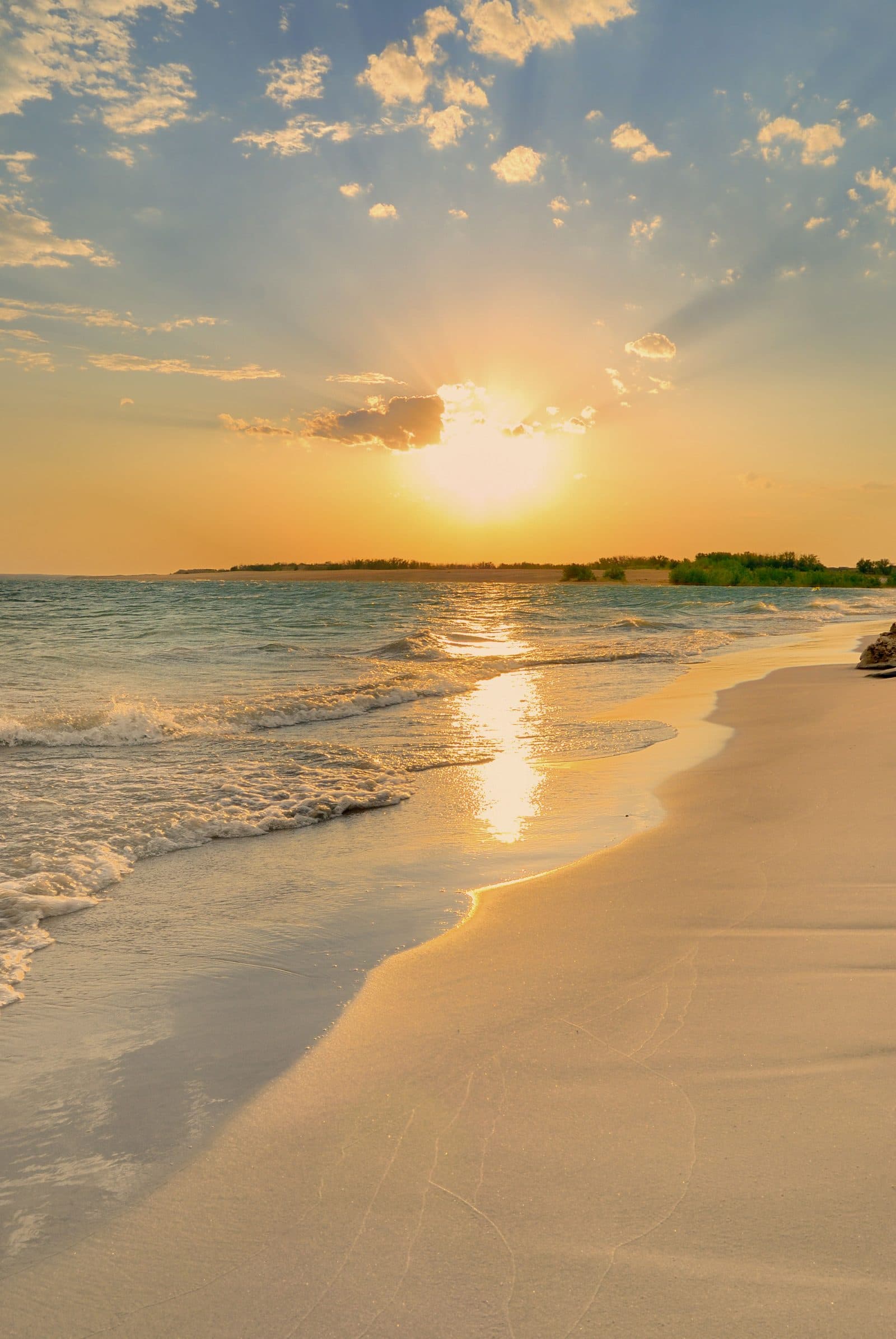 The sun going down over a quiet sandy beach, with small waves washing up the shore